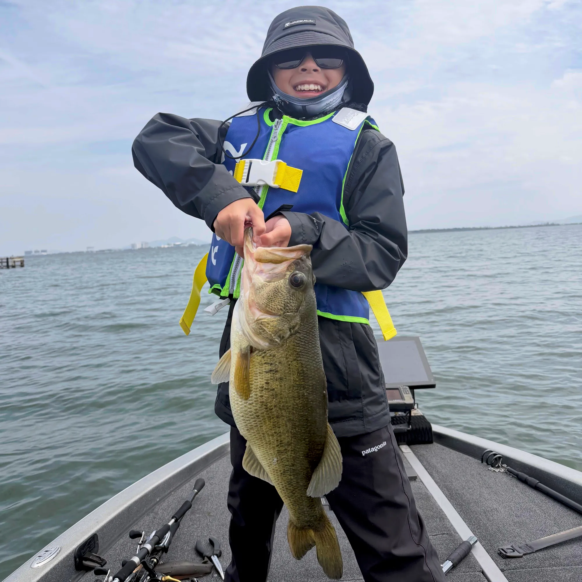 A young guest in a life jacket holding a largemouth bass on the bow of a bass boat
